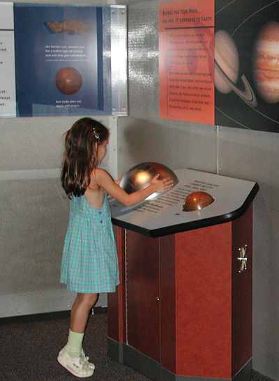 Photograph: a young girl feels a large globe in the gallery